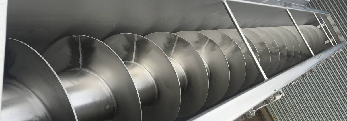 A helical screw flight turning inside an open stainless steel trough conveyor